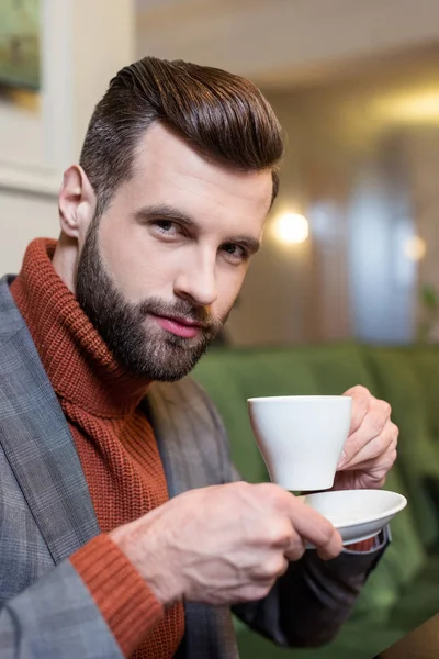 Красивый мужчина в формальной одежде смотрит в камеру и пьет кофе в ресторане — стоковое фото