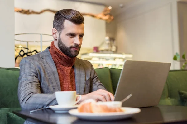Focado homem de negócios bonito no desgaste formal sentado à mesa e digitando no laptop no restaurante — Fotografia de Stock