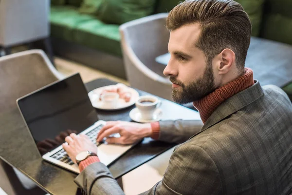 Schöner Geschäftsmann sitzt am Tisch und tippt auf Laptop mit leerem Bildschirm im Restaurant — Stockfoto