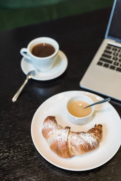 Plate with croissant and sauce, coffee and laptop on table in cafe — Stock Photo