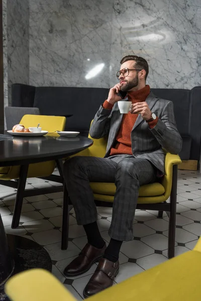Handsome man in formal wear talking on smartphone while drinking coffee in restaurant — Stock Photo