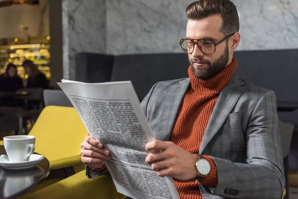 Enfocado hombre con estilo en ropa formal y gafas sentado y leyendo periódico en el restaurante - foto de stock