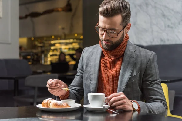 Hombre guapo en ropa formal y gafas sentado a la mesa durante el almuerzo en el restaurante - foto de stock