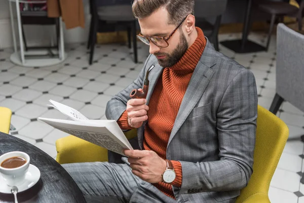 Stylish man in formal wear sitting at table, reading newspaper and smoking pipe in restaurant — Stock Photo