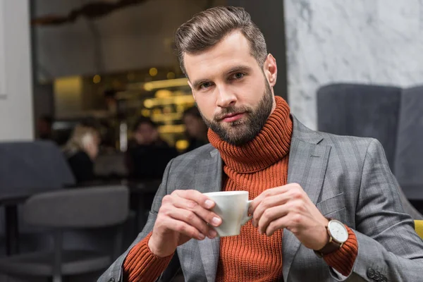 Красивий чоловік у формальному одязі дивиться на камеру і п'є каву в ресторані — стокове фото