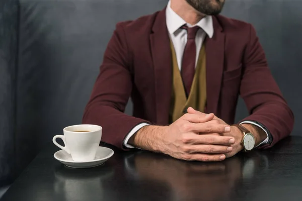 Vista cortada de empresário bonito em desgaste formal sentado à mesa com xícara de café no restaurante — Fotografia de Stock