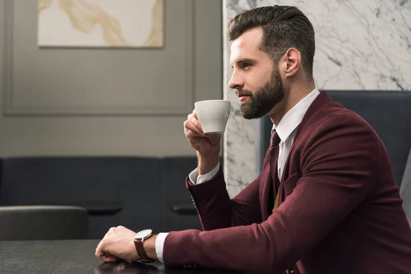 Handsome businessman in formal wear sitting at table and drinking coffee in restaurant — Stock Photo