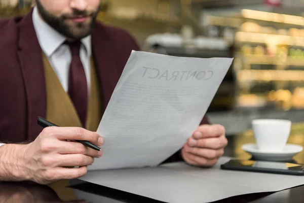 Vista recortada de hombre de negocios en ropa formal sentado en la mesa y mirando el contrato - foto de stock