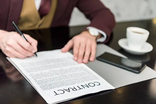 Vista recortada del hombre de negocios en ropa formal sentado a la mesa y la firma del contrato — Stock Photo