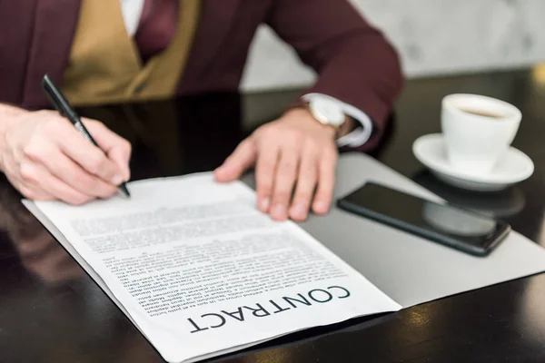 Vista recortada del hombre de negocios en ropa formal sentado a la mesa y la firma del contrato - foto de stock