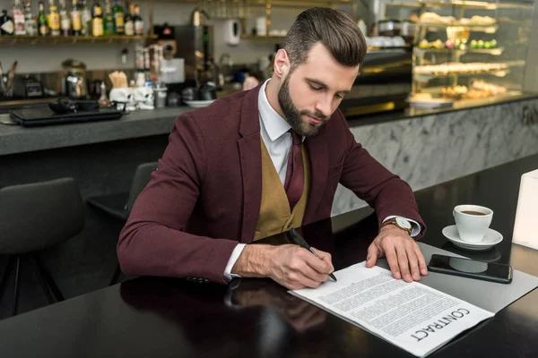 Bel homme d'affaires en tenue de cérémonie assis à table et signant un contrat — Photo de stock