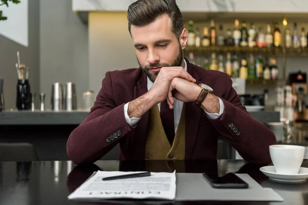 Pensive businessman in formal wear with folded hands sitting at table and looking at contract — Stock Photo