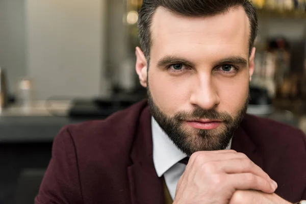 Retrato de hombre de negocios barbudo guapo en ropa formal con las manos dobladas mirando a la cámara - foto de stock