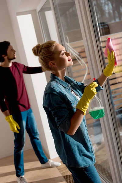 Couple in rubber gloves cleaning window in apartment — Stock Photo