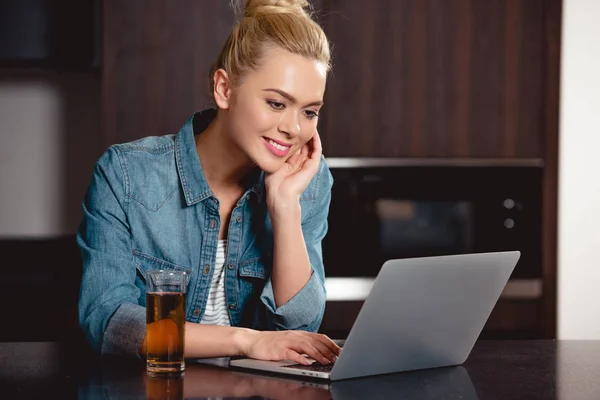 Chica atractiva sonriendo y utilizando el ordenador portátil en casa - foto de stock