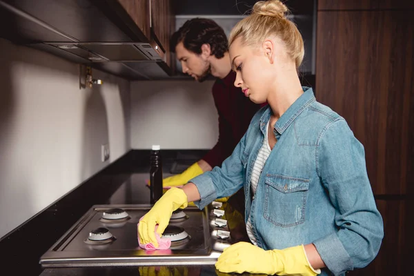 Красивая девушка и красивый мужчина в резиновых перчатках чистят кухню дома — стоковое фото