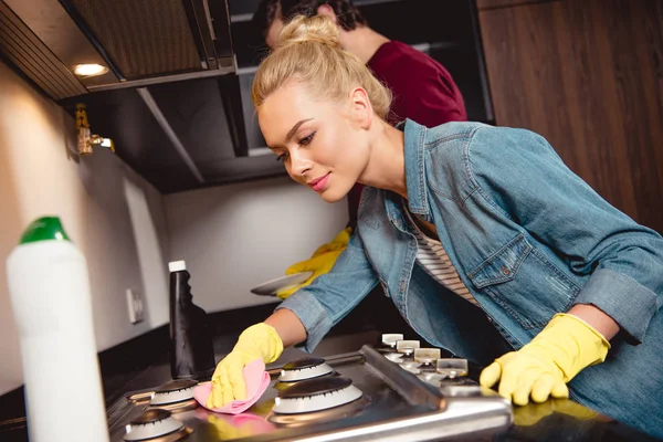 Chica atractiva en guantes de goma cocina de limpieza con el marido lavar los platos - foto de stock