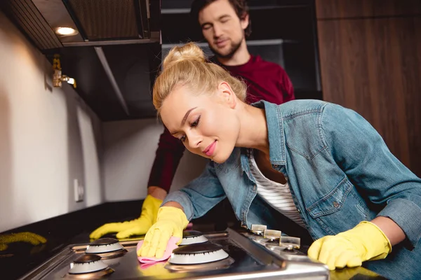 Attractive girl in rubber gloves cleaning kitchen with husband — Stock Photo