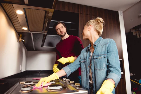 Smiling couple in rubber gloves cleaning kitchen and furniture together and looking at each other — Stock Photo