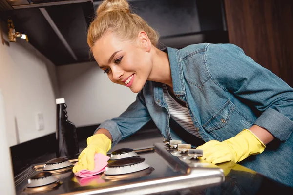 Menina atraente em luvas de borracha sorrindo e limpeza cozinha — Fotografia de Stock