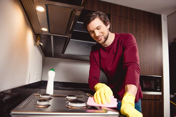 Homem bonito em luvas de borracha limpeza cozinha e sorrindo — Fotografia de Stock