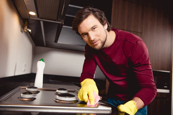 Schöner Mann in Gummihandschuhen putzt Küche und schaut in die Kamera — Stockfoto