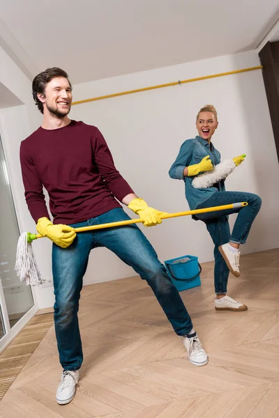 Cheerful family couple in rubber gloves performing with cleaning equipment at home — Stock Photo