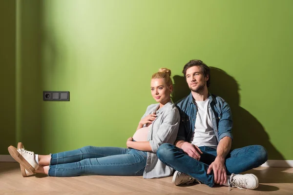 Thoughtful pregnant girl sitting on floor with husband by green wall — Stock Photo