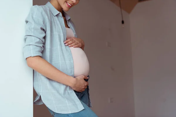 Vista recortada de la mujer embarazada sonriente con las manos en el vientre - foto de stock