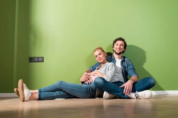 Lächelnder Mann und schwangere Frau sitzen auf dem Boden und schauen in die Kamera — Stockfoto