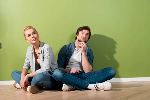 Thoughtful girl with husband sitting on floor by green wall — Stock Photo