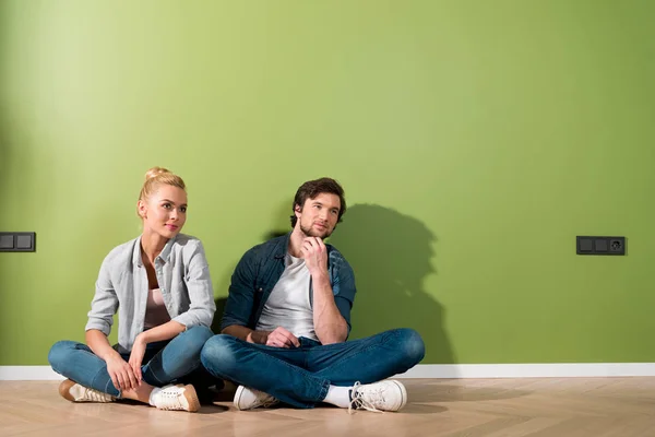 Thoughtful couple sitting on floor by green wall — Stock Photo
