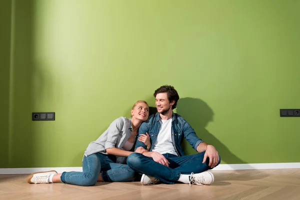 Pareja amorosa sentada en el suelo y mirándose unos a otros por la pared verde - foto de stock