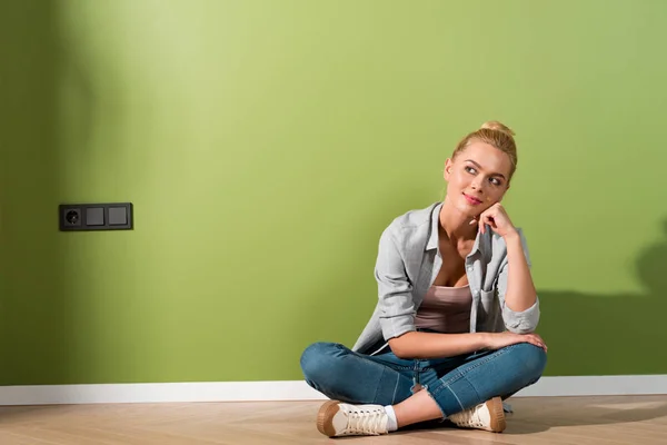 Nachdenkliches Mädchen lächelt und sitzt auf dem Boden an der grünen Wand — Stockfoto