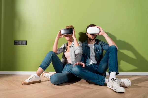 Удивленные девушка и мужчина сидят на полу и держат наушники виртуальной реальности на головах — стоковое фото