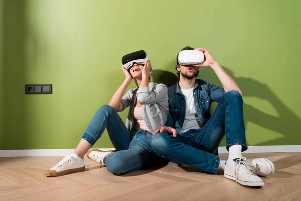 Chica sorprendida y hombre con auriculares de realidad virtual en cabezas sentadas en el suelo — Stock Photo