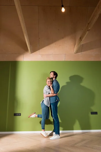 Amorevole coppia di famiglie abbracciati da muro verde in appartamento — Foto stock