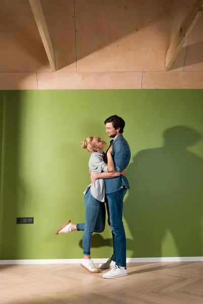 Sorrindo casal abraçando e olhando um para o outro por parede verde — Fotografia de Stock