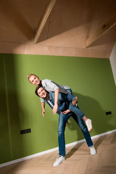 Bel homme donnant piggyback tour à attrayant fille dans l'appartement — Photo de stock