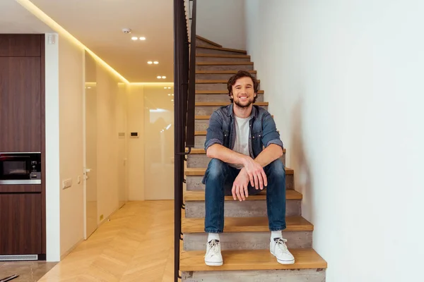 Homem alegre sorrindo e sentado nas escadas em casa — Fotografia de Stock