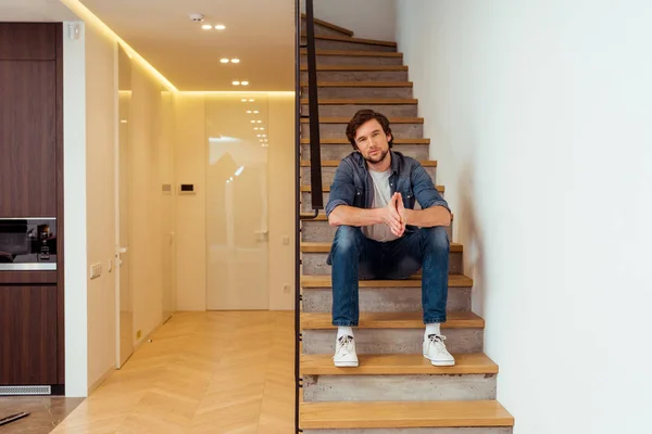 Schöner Mann sitzt auf einer Treppe und schaut in die Kamera — Stockfoto