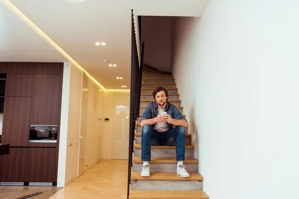 Homem bonito sentado nas escadas e usando smartphone — Fotografia de Stock