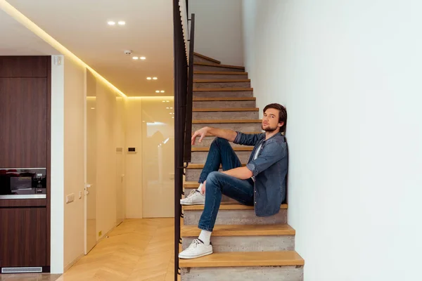 Schöner Mann sitzt auf der Treppe und schaut zu Hause in die Kamera — Stockfoto