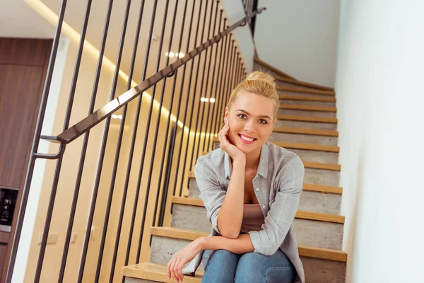 Menina atraente sentado nas escadas, sorrindo e olhando para a câmera — Fotografia de Stock