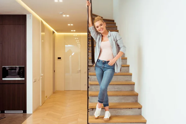 Attraktives Mädchen, das auf der Treppe steht und zu Hause in die Kamera schaut — Stockfoto