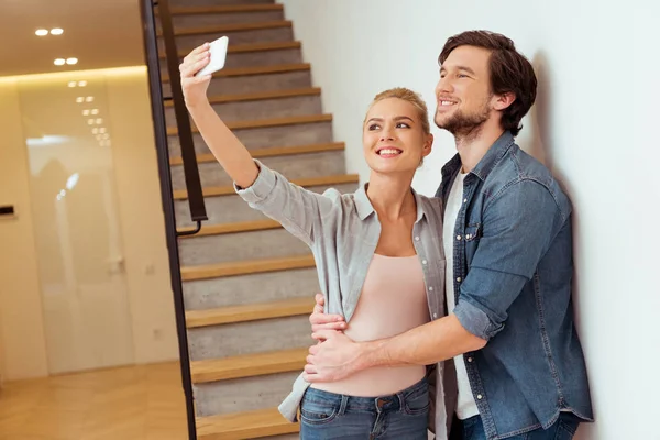 Alegre familia pareja tomando selfie cerca escaleras en casa - foto de stock