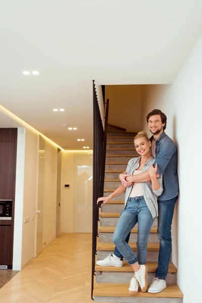 Handsome man standing on stairs and embracing wife — Stock Photo