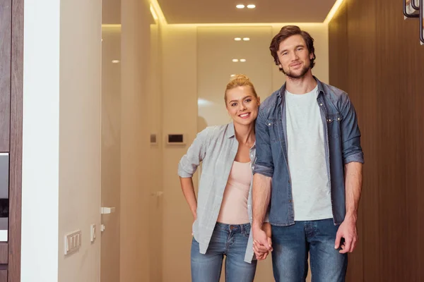 Sonriente pareja cogida de la mano y mirando a la cámara en casa - foto de stock