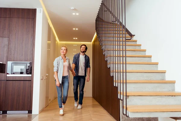 Alegre pareja cogida de la mano cerca de escaleras en casa - foto de stock