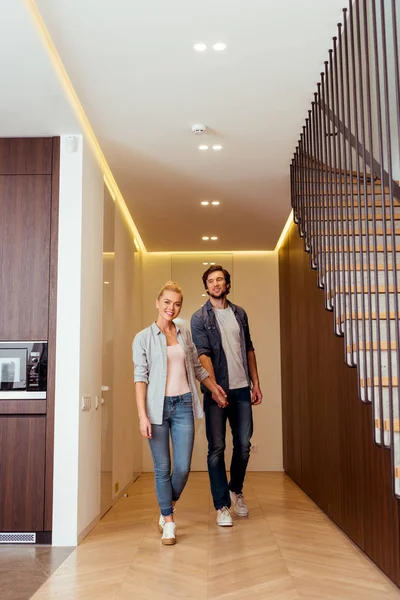 Attractive girl looking at camera and holding hands with husband at home — Stock Photo